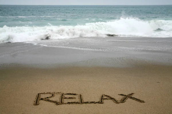 海を背景にビーチサンドで書かれたリラックス — ストック写真