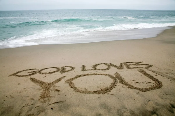 stock image god loves you written in beach sand with the ocean as the background. 