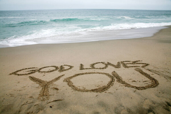 god loves you written in beach sand with the ocean as the basic. 