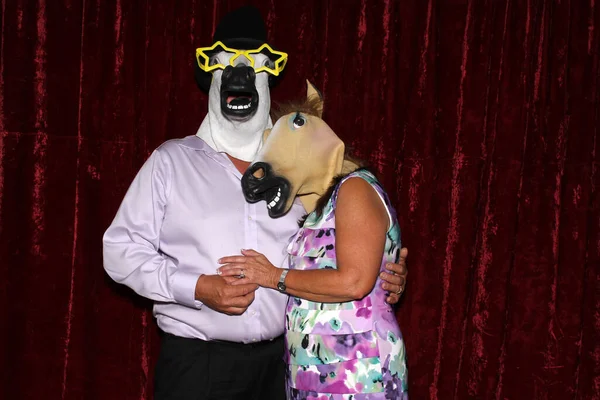 Unidentifiable People wear Horse Head Masks and pose and play while their pictures are taken in a Photo Booth