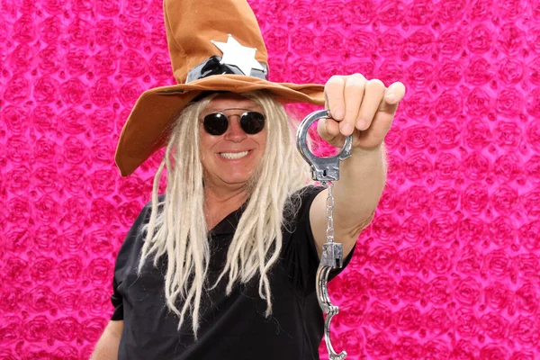 A man wears crazy props and poses for his picture to be taken in a photo booth at a party