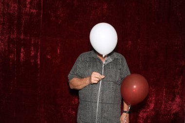 Bir adam bir partide fotoğraf kabininde yüzünü Helium Balonunun arkasına saklar..