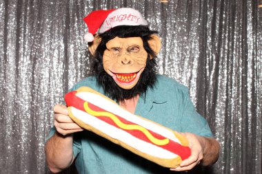 Maymun maskeli bir adam, bir partide fotoğraf kabininde fotoğraf çekilirken aptalca pozlar verir..