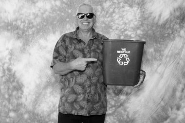 Black and white photo. A man holds a Recycle Trash Bin as he smiles for his picture to be taken. Recycling helps save the planet Earth. Save the Earth, Recycle. Blue Trash Can. Save the Earth.