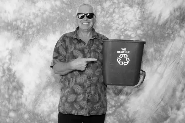 Black and white photo. A man holds a Blue Recycle Trash Bin as he smiles for his picture to be taken. Recycling helps save the planet Earth. Save the Earth, Recycle. Blue Trash Can. Save the Earth.