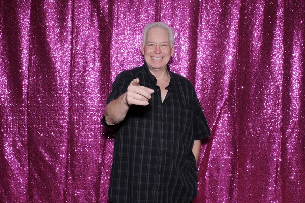 man smiles and points at camera on sequin background. he waits for his pictures to be taken while enjoying a Photo Booth at a Wedding or Party.