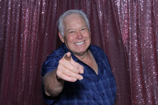 man smiles and points at camera on sequin background. he waits for his pictures to be taken while enjoying a Photo Booth at a Wedding or Party.