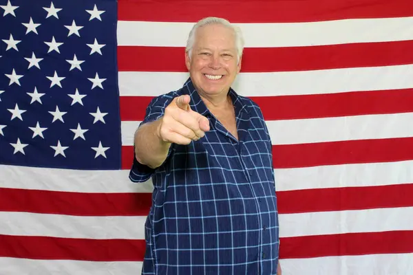 A proud American Man points at camera and Poses in front of the American Flag while waiting for his pictures to be taken while in a photo booth at a Fourth of July Party.