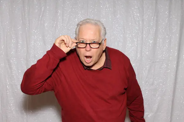 Photo Booth. A man shocked  and poses while in a Photo Booth at a Party. Photo Booth with a white sequin background.