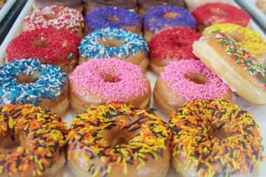 Çörekler. Donut dükkanında satılık renkli çörekler. Kutuda jöleli ve dekore edilmiş çörekler, çeşitli aroma ve malzemeler sergileniyor, canlı krema renkleriyle, ahşap bir masaya dizilmiş, tatlı ya da tatlı için mükemmel..