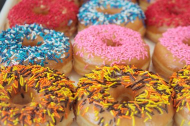 Çörekler. Donut dükkanında satılık renkli çörekler. Kutuda jöleli ve dekore edilmiş çörekler, çeşitli aroma ve malzemeler sergileniyor, canlı krema renkleriyle, ahşap bir masaya dizilmiş, tatlı ya da tatlı için mükemmel..