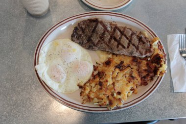 Biftek ve yumurta kahvaltısı. Biftekli kahvaltı, 3 yumurta, haşhaşlı patates, tereyağlı ekşi ekmek ve kremalı kahve. Yiyecek ve içecek. Yiyecekler. Kahvaltıda. Yumurtalar. Biftek. - Kahve. - Şerefe. Esrar Browns. Bıçak. Çatal. Kaşık. Tabak. - Öğle yemeği. Akşam yemeği. Atıştırmalık. 