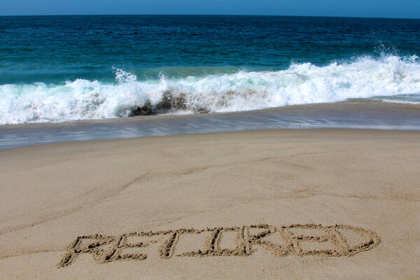 Устал от дел. Слово "пенсионер" написано на песке на пляже. Лагуна Бич, Калифорния. Отставной, написанный на песке. The Beach is a great place when you are Retired. 