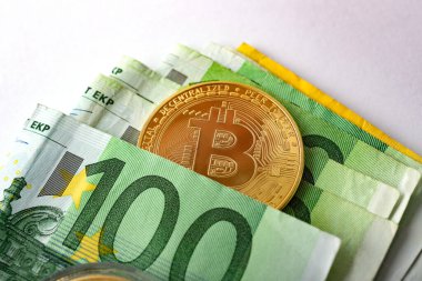 Beyaz arkaplan üzerinde avro banknotları olan Bitcoin altın sikkeleri, yakın plan görüntü.