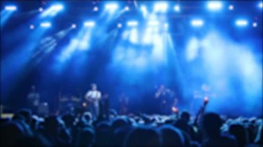 Canlı müzik etkinliği. Konserde kalabalık el kaldırıyor ve arka planda parlak sahne ışıkları var.,