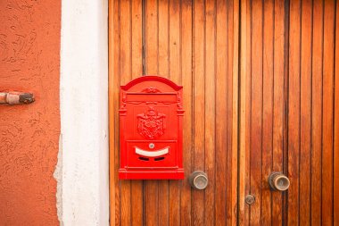 Caddedeki bir evin ahşap kapısında postaların teslim edilmesini bekleyen klasik kırmızı posta kutusu.