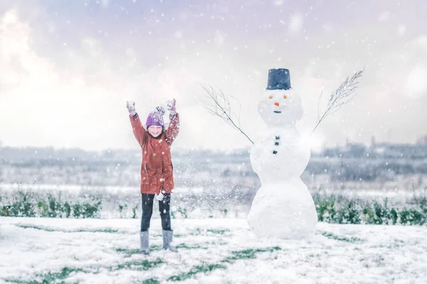 Girl cheering with a snowman in the snow on a winter day in December