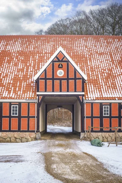 Red farm house with an open gate in the winter with a clock and a bell