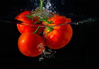 Suya düşen taze kırmızı domates. Su sıçraması ve siyah arka planda izole edilmiş hava kabarcıkları..