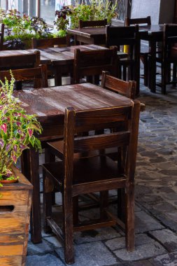 Islak, boş masa ve yağmur sırasında açık hava kafeteryasının terasında sandalyeler. Yağmur altında sokak şehri hayatı.