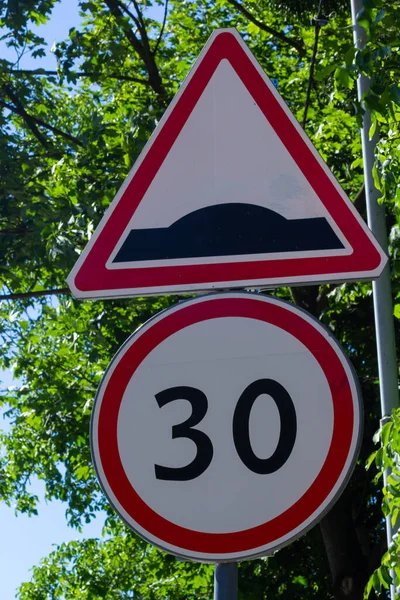 rough road sign and speed limit on a background of green trees and blue sky.