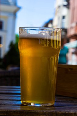 Ahşap masada soğutulmuş bir bardak bira. Arka planda bulanık bir yazlık var.