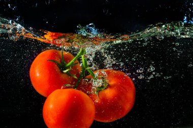 Suya düşen taze kırmızı domates. Su sıçraması ve siyah arka planda izole edilmiş hava kabarcıkları..