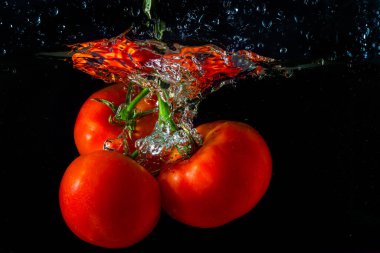 Suya düşen taze kırmızı domates. Su sıçraması ve siyah arka planda izole edilmiş hava kabarcıkları..