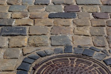 Eski metal kanalizasyon kapağı dışarı pürüzsüz bir kaldırım taşı atılmıştır yolun ortasında.