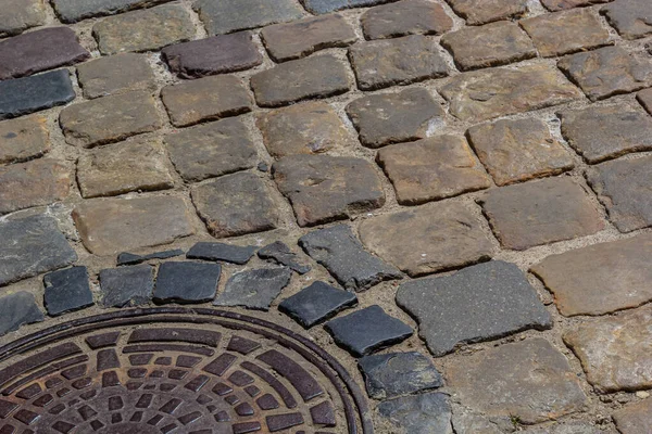 Eski metal kanalizasyon kapağı dışarı pürüzsüz bir kaldırım taşı atılmıştır yolun ortasında.