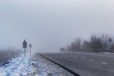 Driver of almost empty grey foggy misty rainy highway intercity road with low poor visibility on cold spring autumn morning. Seasonal bad rainy weather accident danger warning. car fog light.