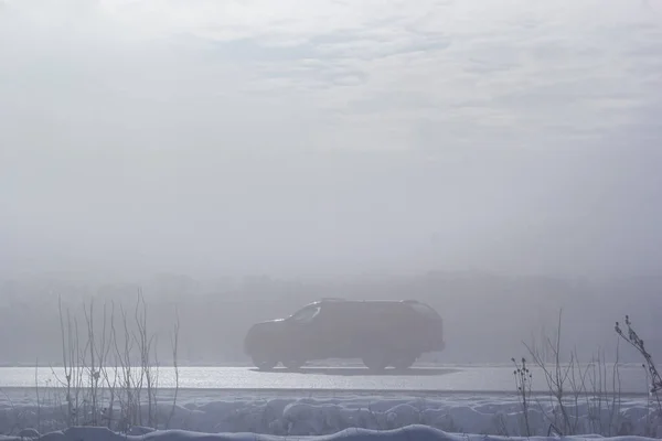 Passenger car in the fog on a winter road with large snowdrifts on the side of the road.