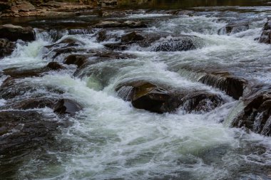 Nehir torrentinin üstündeki soyut dokuya yakın çekim ve güneşli bir günde vadideki kayalıklarda köpük ve kabarcıklarla akan temiz soğuk su. Doğa gücü ve güç arkaplanı.