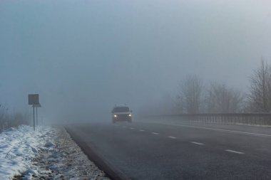 Driver of almost empty grey foggy misty rainy highway intercity road with low poor visibility on cold spring autumn morning. Seasonal bad rainy weather accident danger warning. car fog light.