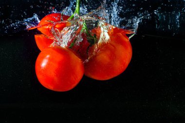 Suya düşen taze kırmızı domates. Su sıçraması ve siyah arka planda izole edilmiş hava kabarcıkları..