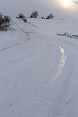 Gün batımında karla kaplı kırsal alanda bir yol. Güneşli kış günü.
