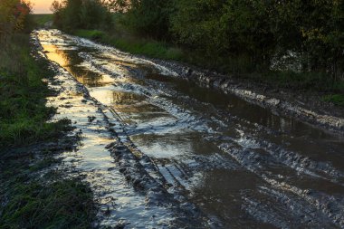 Günbatımında köyde derin rutubet ve su birikintileriyle kaybolan toprak yol..