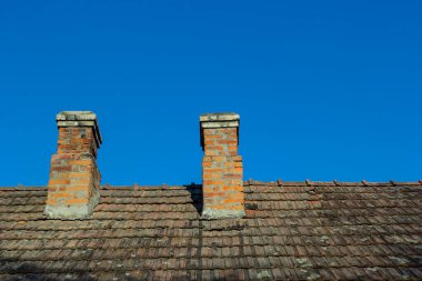 Köy evinin tepesindeki kırmızı tuğladan baca. Gökyüzünün arka planında fayanslardan yapılmış bir çatı.