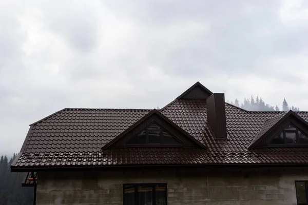 House with new brown metal tile roof and rain gutter. Metallic Guttering System, Guttering and Drainage Pipe Exterior.