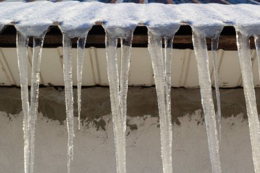 Keskin buz saçakları ve çatısından sarkan erimiş kar. Güzel şeffaf buz saçakları yavaşça bir çatının üzerinde süzülüyor..