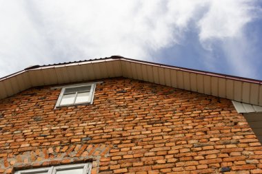 Pencereli kırmızı tuğla duvar. Gökyüzünün arka planında bulutlu alt görünüm.