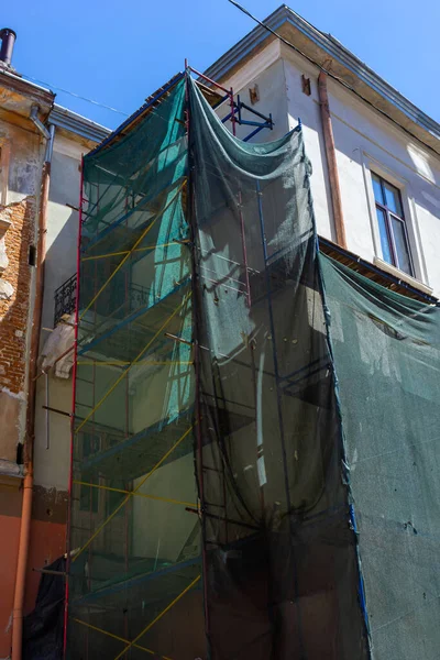 stock image Restoration of the building. Scaffolding and protective green building mesh. Safety techniques during construction works.