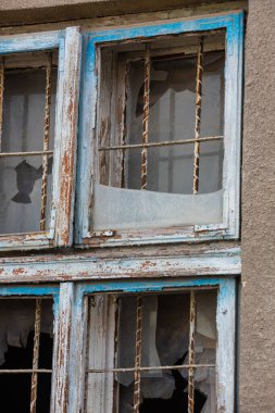 Eski bir evin dış duvarında yıpranmış ahşap panjurları ve kırık camları olan eski bir pencere..