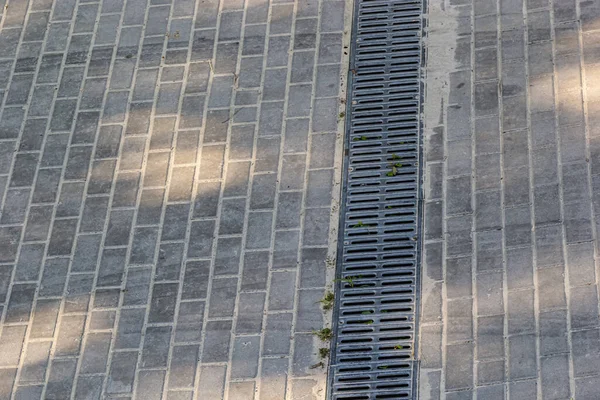 A lattice of a drainage paving system on a footpath made of square stone tiles, close up of a rainwater drainage system.