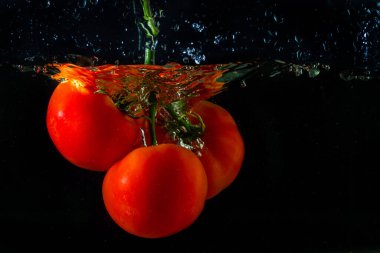 Suya düşen taze kırmızı domates. Su sıçraması ve siyah arka planda izole edilmiş hava kabarcıkları..
