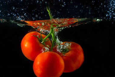 Suya düşen taze kırmızı domates. Su sıçraması ve siyah arka planda izole edilmiş hava kabarcıkları..