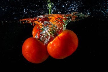 Suya düşen taze kırmızı domates. Su sıçraması ve siyah arka planda izole edilmiş hava kabarcıkları..