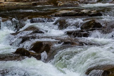 Nehir torrentinin üstündeki soyut dokuya yakın çekim ve güneşli bir günde vadideki kayalıklarda köpük ve kabarcıklarla akan temiz soğuk su. Doğa gücü ve güç arkaplanı.