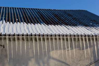 Keskin buz saçakları ve çatısından sarkan erimiş kar. Güzel şeffaf buz saçakları yavaşça bir çatının üzerinde süzülüyor..