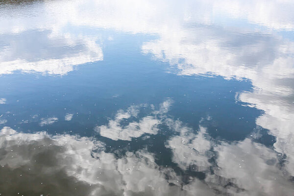 Calm water surface. Summer evening near a forest lake, the surface of the water is smooth, with small waves. The sky with clouds is reflected from the surface, coloring the water in different colors.